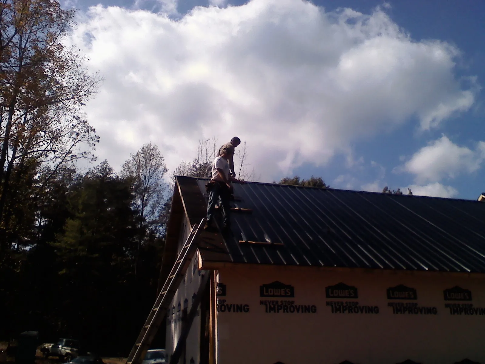 Roofer fastening dark metal panels high against a cloudy sky in Huntington