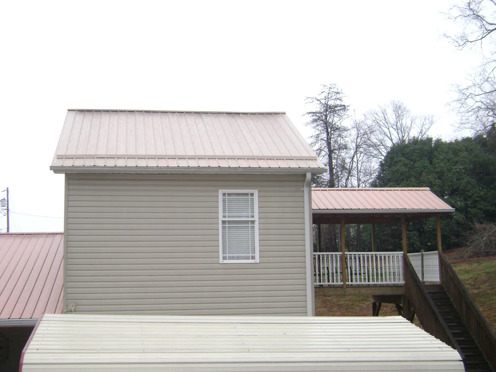 Tan metal roofs on a two story addition and attached porch, from a Roof Replacement job in Huntington